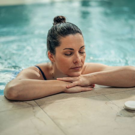 Woman relaxes in 5* resort pool with closed eyes and folded arms close up