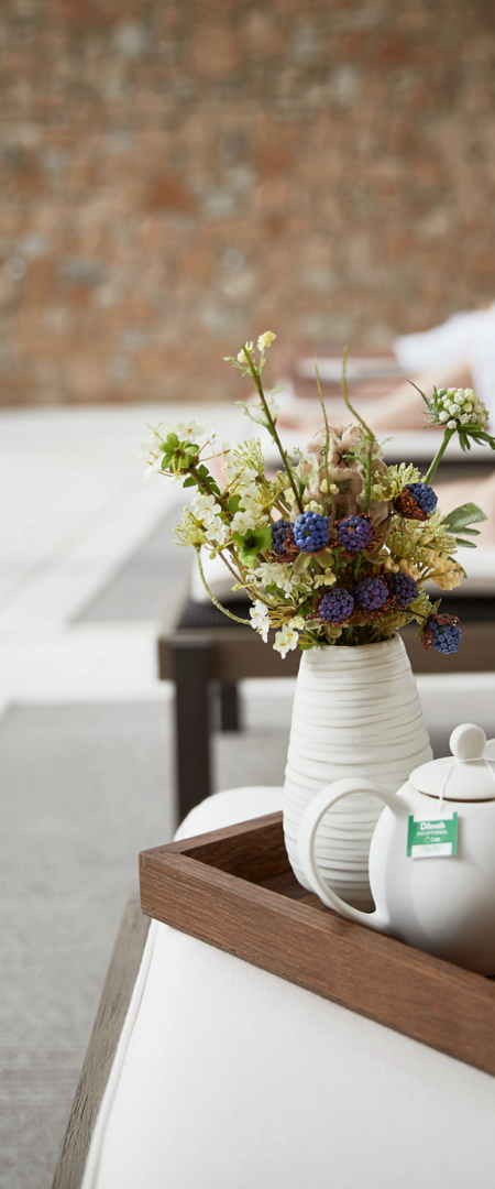 Tea pot on wooden tray with small vase of flowers on day bed at luxuty 5* hotel in Girona