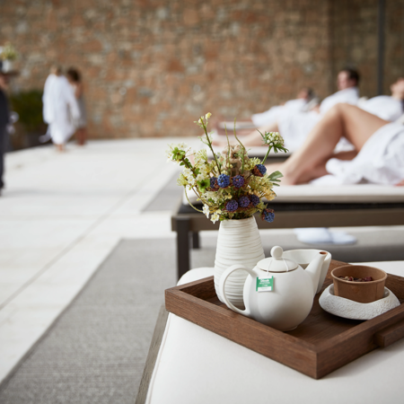 Tea pot on wooden tray with small vase of flowers on day bed at luxuty 5* hotel in Girona