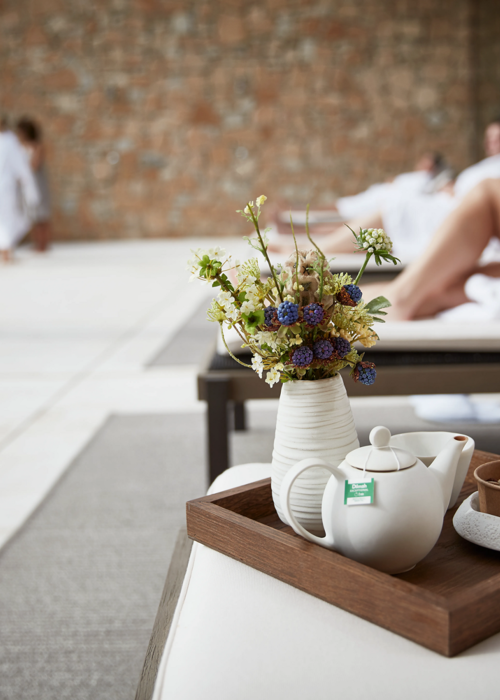 Tea pot on wooden tray with small vase of flowers on day bed at luxuty 5* hotel in Girona