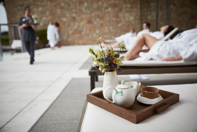 Tea pot on wooden tray with small vase of flowers on day bed at luxuty 5* hotel in Girona