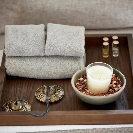 Small candle and grey towels on wooden tray at luxury wellness spa.