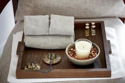 Small candle and grey towels on wooden tray at luxury wellness spa.