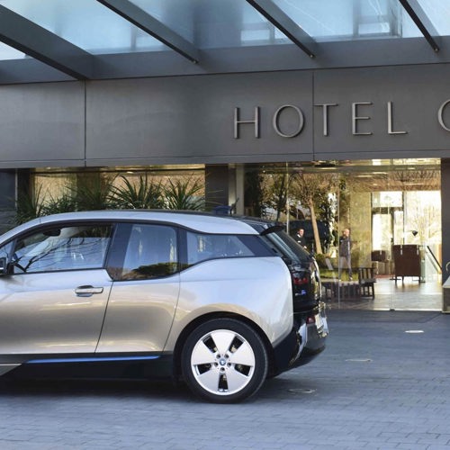 A sleek silver BMW electric car parked at the luxury Hotel Camiral entrance.