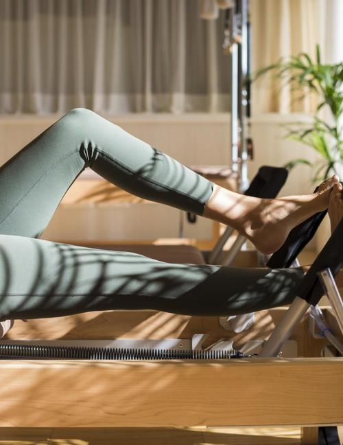 Woman on reformer pilates machine in green yoga pants at the Camiral.