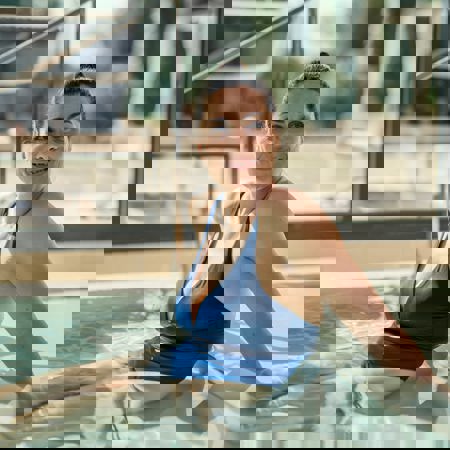 Woman relaxes in 5* Camiral Resort pool with blue swimsuit while smiling