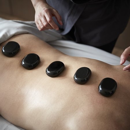 Hot stone back massage with black stones and therapists hands