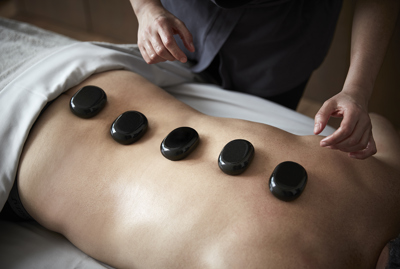Hot stone back massage with black stones and therapists hands