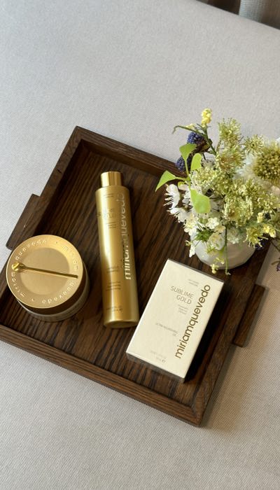 Gold Miriam Quevedo beauty products on elegant wooden tray on grey cushion
